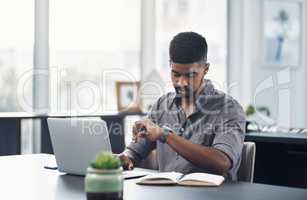 Good time management allows you to accomplish more. Shot of a young businessman checking the time while working on a laptop in an office.