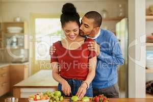 Supporting each other in being the healthiest they can be. Shot of a young man kissing his wife while she prepares a healthy snack at home.