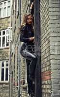 The perfect secret agent. Seductive young woman climbing a wall while wearing a catsuit - portrait.
