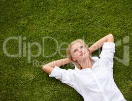So much to ponder.... High angle shot of an attractive young woman relaxing on a grassy field and looking up at the sky.