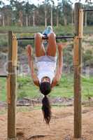 Strengthening her core. A young woman hanging upside down by her legs and using her core to pull herself up.