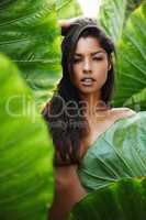 Topless in the tropics. Gorgeous young ethnic woman hiding her topless body behind a green leaf.