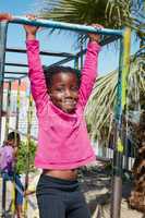Holding on tight to carefree days of youth. Portrait of a happy little girl hanging on a jungle gym.