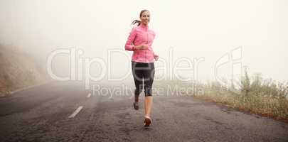 The miles are rolling away behind her. Shot of a young woman jogging on a country road on a misty morning.