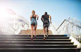 Stepping up their fitness. Rearview shot of two young people jogging up an outdoor flight of stairs.