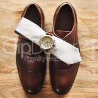 Classic never goes out of fashion. Still life shot of a wristwatch and tie on top of formal shoes on a wooden surface.