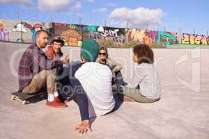 Sharing their common interests. Shot of a group of friends hanging out in the sun at a skate park.