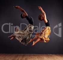 Synchronisity. Two contemporary dancers performing a synchronized leap in front of a dark background.