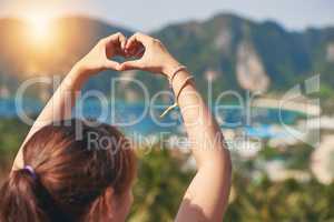This island has stolen her heart. Rearview shot of a happy young tourist making a heart with her hands against a beautiful landscape.