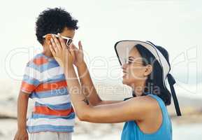 Sunglasses are really helpful for protecting your eyes. Shot of a mother applying sunscreen to her son at the beach.