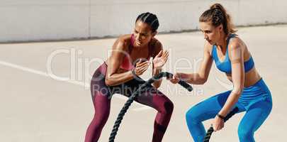 Your achievement is worth those tough lessons. Shot of sporty young woman doing heavy rope training with her trainer.