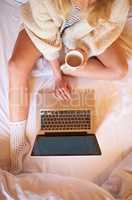 Coffee, comfort and connectivity. Shot of an unidentifiable woman using her laptop while enjoying a cup of coffee in bed.