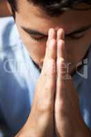 Hoping and praying. Closeup of a young man praying with his hands together.