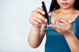 Stay in the know and knock that diabetes. Studio shot of a young girl using a blood sugar test on her finger against a gray background.