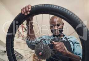 Sometimes, all you need is a new part. Shot of a handsome young man standing alone in his shop and repairing a bicycle wheel.