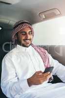 En route to success. Shot of a young muslim businessman using his phone while traveling in a car.