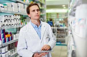 Digitizing drug store management duties. Shot of a young pharmacist using a digital tablet in a pharmacy.