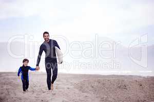 The waves are waiting, lets go. A father walking along the beach with his young son before a surfing lesson.