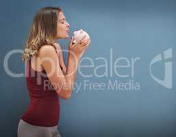 Please let there be money in here.... Shot of a young woman kissing a piggybank against a gray background.