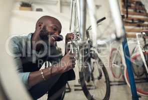 Im almost done fixing this. Shot of a handsome young man crouching alone in his shop and repairing a bicycle wheel.