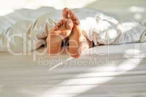 Wiggling toes of wakefulness. Shot of a mans feet poking out from the bottom of his bed.