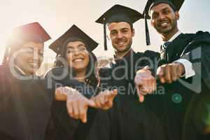 You too can become outstanding. Portrait of a group of students pointing forward on graduation day.