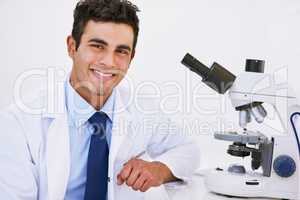 Finding solutions in the small things. Portrait of a smiling lab technician using a microscope while sitting in a lab.