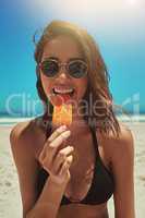 Cool off this summer. Portrait of a sexy young woman enjoying an ice lolly at the beach.