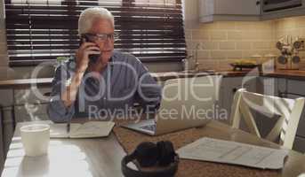 Old age hasnt stopped me from working. Shot of a senior man sitting alone in the kitchen and using technology to work from home.