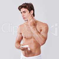 Freshening up. Studio shot of a handsome bare chested young man applying lotion to his face.