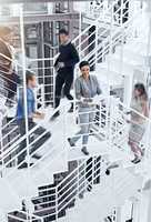 This office barely stands still. Portrait of a young professional standing on a stairs with colleagues rushing around her.