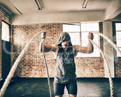 Ropes arent just for tying things. Shot of a hooded and determined young man making use of ropes to workout in the gym.