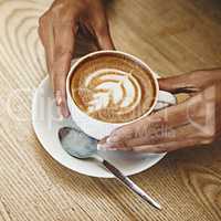 This is the best coffee youll ever have. Cropped shot of an unrecognizable woman sitting alone in a cafe and holding a cup of cappuccino.