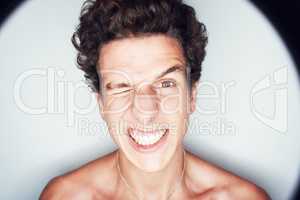 Feeling quirky. Close up portrait of a young man grinning with a scrunched up face while being surrounded by a halo of light.