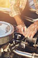 Making a few minor adjustments. Shot of a senior man looking under the hood of his car while on a roadtrip.