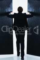 Opening the door to business success. Rear view shot of a businessman opening the doors of a dark room.