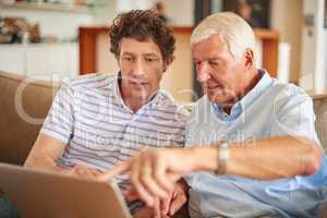 Explain that part to me again.... Shot of a man and his father sitting with a laptop indoors.