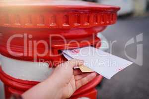 The old fashioned way of messaging. Closeup of an unrecognizable persons hand sliding in letters into a red mailbox outside during the day.