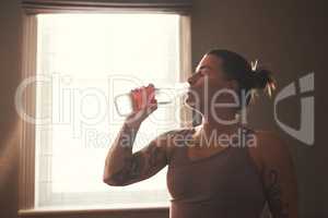 Good hydration is key. Shot of a young woman drinking water after her workout at home.