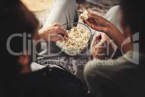 Gotta be love if Im sharing popcorn. Rearview shot of a young couple sitting on sofa snacking on popcorn together at home.