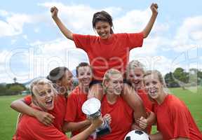 We are the champions. Portrait of an all-girls soccer team raising their captain in triumph.