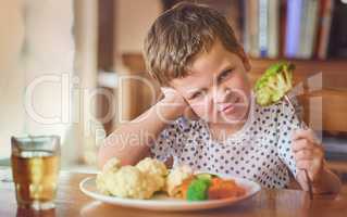 Theres no way Im eating this stuff. Portrait of a disgusted little boy refusing to eat his vegetables at the dinner table.