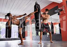 Harder man. Shot of a two young men practicing kickboxing in a gym.