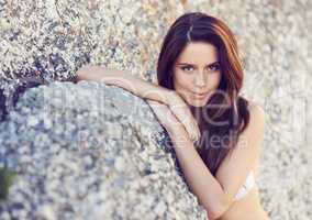 Shes simply smoldering.... A gorgeous young woman in a bikini leaning against a boulder.