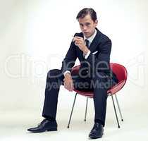 Suave smoker. A studio portrait of a handsome young gentleman in a pinstripe suit sitting on a chair.