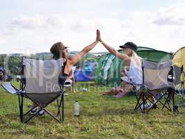 Happy campers. Rearview shot of two friends giving each other a high five at an outdoor festival.