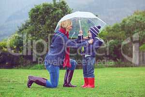 Making sure hes covered up. Full length shot of a mother making sure her son is covered while outside in the rain.