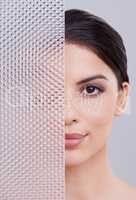 Introducing flawless skin. Shot of a beautiful young woman with her face partially obscured through a plastic panel.