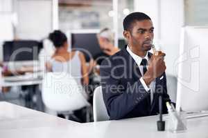 Getting his fix without leaving his desk. A young businessman smoking an electronic pipe indoors.