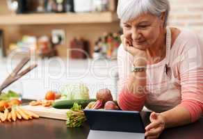 I love these cooking channels. Shot of a woman resting her chin on her hands as she watches a tablet in her kitchen.